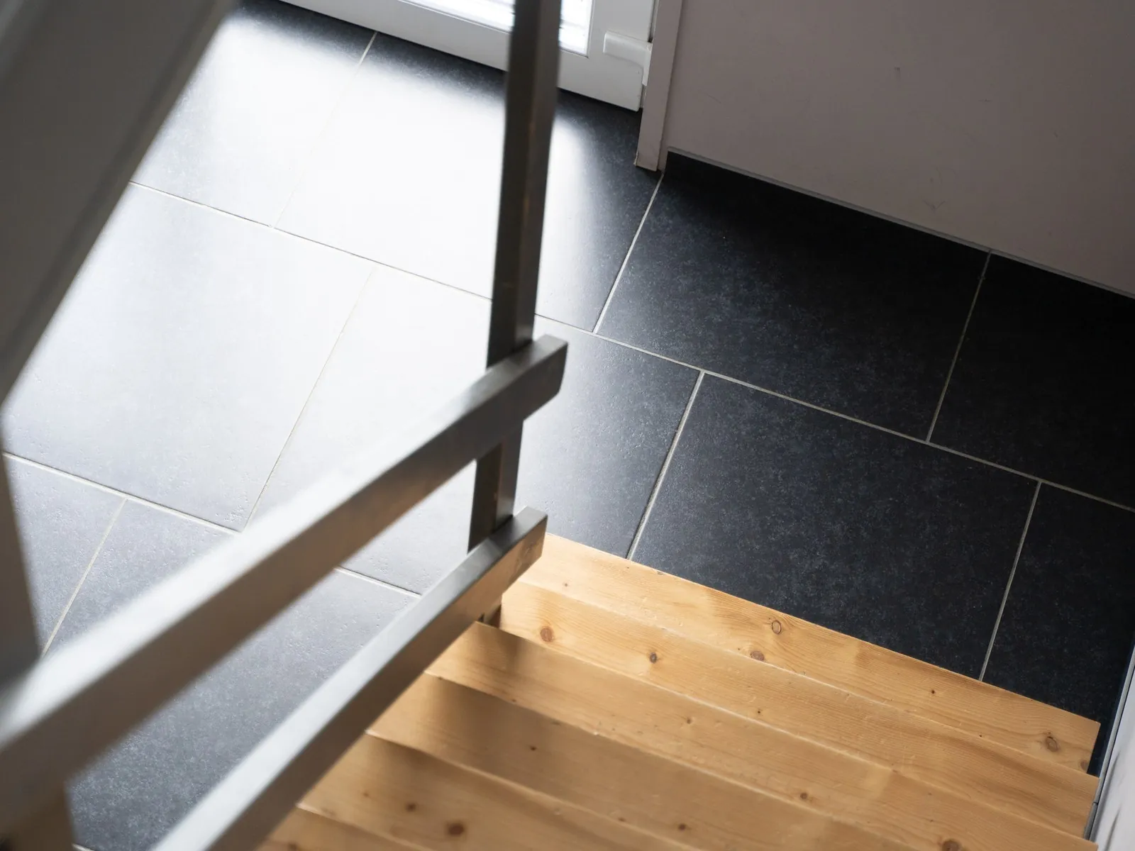 Escalier vu de dessus : dalles anthracite, marches en bois clair, limon et garde-corps en acier noir
