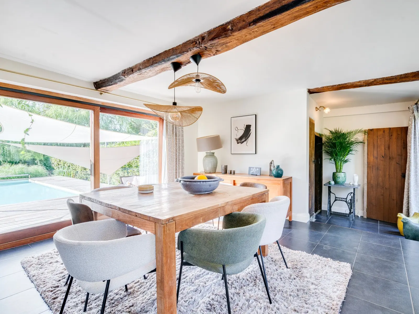 Salle à manger d'une grange restaurée : table de chêne, poutre ancienne, baie ouverte sur la piscine